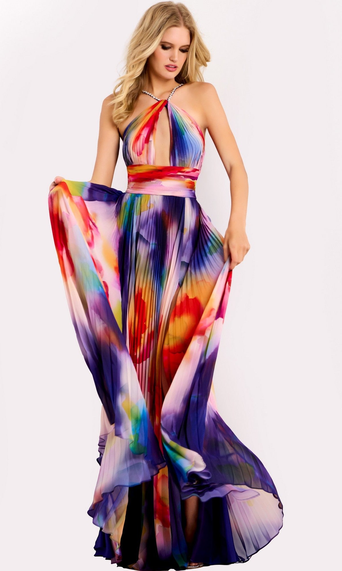 A woman wears the Jovani 42717 long prom dress, featuring a colorful abstract pattern, pleated A-line skirt, and halter neckline.